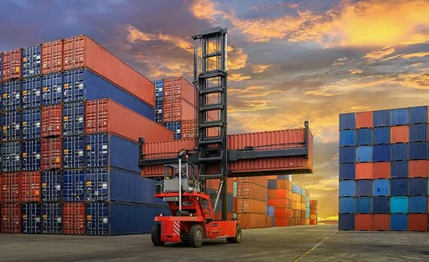 Container stacks and a reach stacker at sunset.
