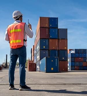 An inspector in a safety vest checking container stacks.